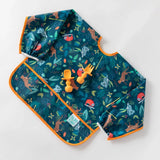 Bumkins Sleeved Bib: Jungle lays on a white background with orange baby utensils on top.