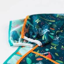 Load image into Gallery viewer, Close-up of Bumkins Sleeved Bib: Jungle on top of a blue bib on a white background, with focus on the elastic cuffs on the sleeve.