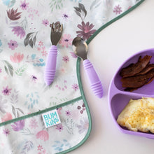 Load image into Gallery viewer, Close-up of Bumkins Sleeved Bib: Floral on a white background, with purple utensils on top and a purple plate of bacon and eggs nearby.