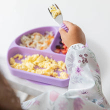 Load image into Gallery viewer, Close-up of a child's arm in Bumkins Sleeved Bib: Floral, holding a fork with scrambled eggs while eating from a purple plate.