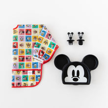 Load image into Gallery viewer, Bumkins Sleeved Bib: Mickey & Friends Check Mates is shown folded on a white background next to a Mickey-shaped plate and matching utensils.