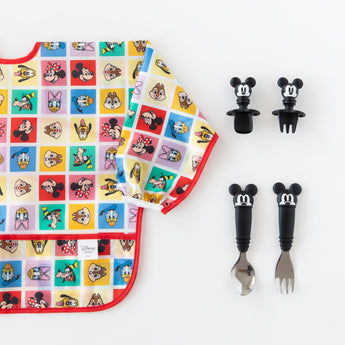 Bumkins Sleeved Bib: Mickey & Friends Check Mates is shown on a white background with two sets of Mickey-shaped utensils.