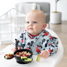 Load image into Gallery viewer, A baby in a high chair wearing a bib eats oatmeal, berries, & avocado from a Bumkins Silicone First Feeding Set: Mickey Mouse Classic Black.