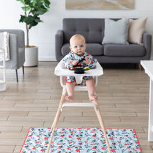 Load image into Gallery viewer, A baby in a Bumkins Sleeved Bib: Mickey Mouse eats from a black bowl in a high chair with a matching mat on the floor underneath.