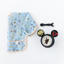 Load image into Gallery viewer, Bumkins Sleeved Bib: Mickey + Minnie Sunny Side Up is folded next to a Mickey-shaped bowl with yogurt and fruit and spoon on a white background.