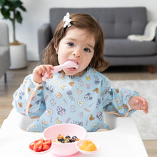 Load image into Gallery viewer, A child in a Bumkins Sleeved Bib: Mickey + Minnie Sunny Side Up enjoys fruit with a spoon, embracing baby-led weaning in a high chair.