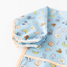 Load image into Gallery viewer, Close-up of Bumkins Sleeved Bib: Mickey + Minnie Sunny Side Up on a white background, showcasing the white elastic cuff on the sleeve.