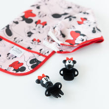 Load image into Gallery viewer, Bumkins Sleeved Bib: Minnie Mouse lays folded next to Minnie Mouse-shaped utensils on a white background.