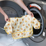 A person holds Bumkins Sleeved Bib: Winnie Loves Hunny in front of an open front-loading washing machine.