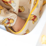 Close-up of child's hand in the front pocket of a Bumkins Sleeved Bib: Winnie Loves Hunny.
