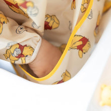 Load image into Gallery viewer, Close-up of child's hand in the front pocket of a Bumkins Sleeved Bib: Winnie Loves Hunny.