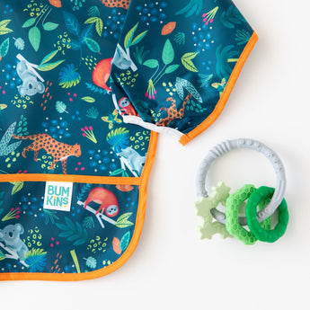 Bumkins Silicone Teething Charms: Green lays next to a blue animal-patterned sleeved bib on a white background.