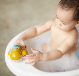 A baby plays with a PlanToys Wooden Submarine Bath Toy, exploring an underwater world surrounded by bubbles.