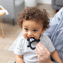 Load image into Gallery viewer, A curly-haired toddler bites a Bumkins Silicone Flat Teether: Mickey Mouse while sitting on an adult's lap indoors.