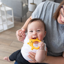 Load image into Gallery viewer, A baby smiles on a woman's lap, happily chewing a Bumkins Silicone Flat Teether: Winnie the Pooh.