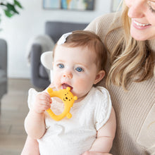 Load image into Gallery viewer, A baby with blue eyes chews on a Bumkins Silicone Flat Teether: Winnie the Pooh for teething relief, held by a smiling blonde woman.