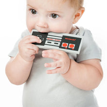 Load image into Gallery viewer, A baby in a gray shirt chews on a Bumkins Silicone Teether: NES™ Controller on a white background.