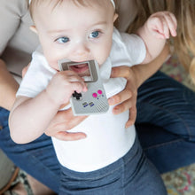 Load image into Gallery viewer, A seated adult holds a child chewing a Bumkins Silicone Teether: Game Boy™.