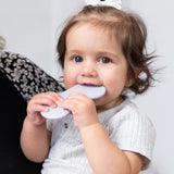 A brown-haired toddler in a light gray shirt chews on a Bumkins Silicone Teether: Nintendo SNES™ Controller for gum relief.