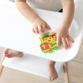 Close-up of a child holding a Bumkins Silicone Teether: Zelda™ Link on a white high chair tray.