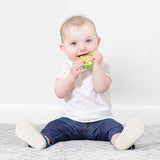 A baby on a carpet in white and blue clothes chews a Bumkins Silicone Teether: Zelda™ Link.