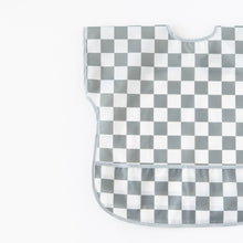 Load image into Gallery viewer, Bumkins Junior Bib: Charcoal Check, with easy-wipe waterproof fabric and a curved neckline, lays flat on a white background.