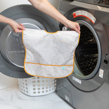 Load image into Gallery viewer, A person holds a Bumkins Junior Bib: Wander in front of a front-loading washing machine.