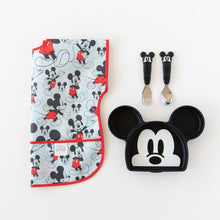 Load image into Gallery viewer, Bumkins Junior Bib: Mickey Mouse Classic lays folded next to a Mickey Mouse-shaped plate and matching utensils on a white background.