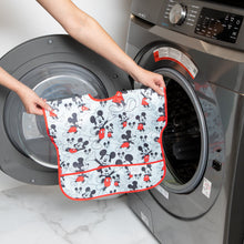 Load image into Gallery viewer, A person holds Bumkins Junior Bib: Mickey Mouse Classic in front of an open front-loading washing machine.