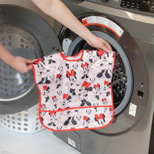 Load image into Gallery viewer, A person holds Bumkins Junior Bib: Minnie Mouse Classic in front of an open front-loading washing machine.