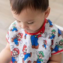 Load image into Gallery viewer, Close-up of a boy wearing a Bumkins Junior Bib: Super Mario™ & Luigi, looking down.