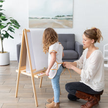 Load image into Gallery viewer, In a cozy room with wall art and plants, a woman adjusts a Bumkins Short-Sleeved Smock: Wander on a girl ready to paint at her easel.