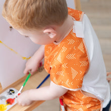 Load image into Gallery viewer, A child painting at an easel in a wearing a Bumkins Short-Sleeved Smock: Grounded, holding a brush.