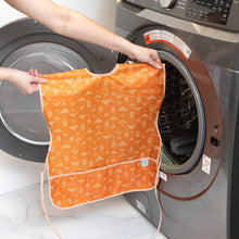 Load image into Gallery viewer, A person holds a Bumkins Short-Sleeved Smock: Grounded in front of an open front-loading washing machine.
