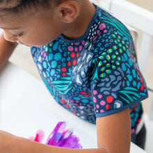 Load image into Gallery viewer, A child paints on paper in while wearing a Bumkins Short-Sleeved Smock: Animal Prints.