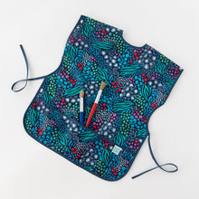 Load image into Gallery viewer, Bumkins Short-Sleeved Smock: Animal Prints lays on a white background, holding two paintbrushes in the pocket.
