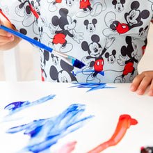 Load image into Gallery viewer, Close-up of a child painting in blue, wearing a Bumkins Short-Sleeved Smock: Mickey Mouse Classic.