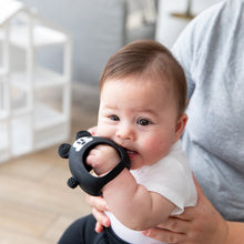 Load image into Gallery viewer, A baby in a white shirt chews on a Bumkins Silicone Un-Droppable Mitt Teether: Mickey Mouse while sitting on an adult's lap indoors.