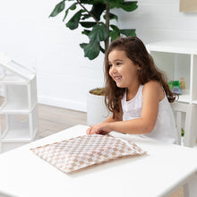 Load image into Gallery viewer, A girl smiles indoors with a Roamio by Bumkins Wet Bag: Sand Check on a white table, with a plant in the background.
