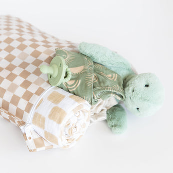 Roamio by Bumkins Wet Bag: Sand Check holds a rolled blanket, green pacifier, clothes, and plush turtle on a white background.