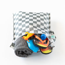 Load image into Gallery viewer, Bumkins Wet Bag: Charcoal Check is packed with a towel, toy dinosaur, flip-flops, and a blue water bottle peeking out on a white background.