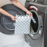 A person holds Bumkins Wet Bag: Charcoal Check in front of an open front-loading washing machine.