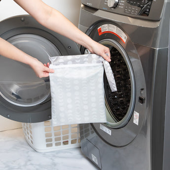 A person holds Bumkins Wet Bag: Lunar Phase in front of an open front-loading washing machine.