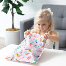 Load image into Gallery viewer, A young blonde girl opens a colorful Roamio by Bumkins Wet Bag: Boots at a white table in a bright room with a nearby potted plant.
