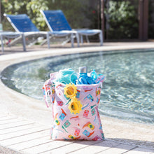 Load image into Gallery viewer, Roamio by Bumkins Wet Bag: Boots holds yellow sunglasses, a towel, water bottle, swimwear, & goggles poolside; empty lounge chairs behind.