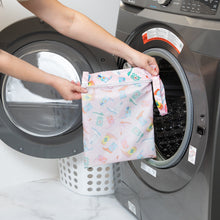 Load image into Gallery viewer, A person holds a Roamio by Bumkins Wet Bag: Boots in front of an open front-loading washing machine.