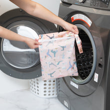 Load image into Gallery viewer, A person holds a Bumkins Wet Bag: Yoga Pals in front of an open front-loading washing machine.