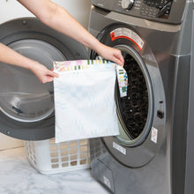 Load image into Gallery viewer, A person holds Roamio by Bumkins Wet Bag: Motley Check in front of an open front-loading washing machine.