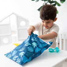 Load image into Gallery viewer, A boy eagerly opens a Bumkins Wet Bag: Blue Tropic at a white table, with a pair of blue goggles close by.