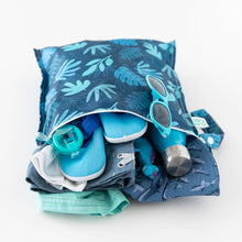 Load image into Gallery viewer, Bumkins Wet Bag: Blue Tropic holds a swimsuit, sun hat, goggles, water shoes, sunglasses, and a dinosaur toy on a white background.
